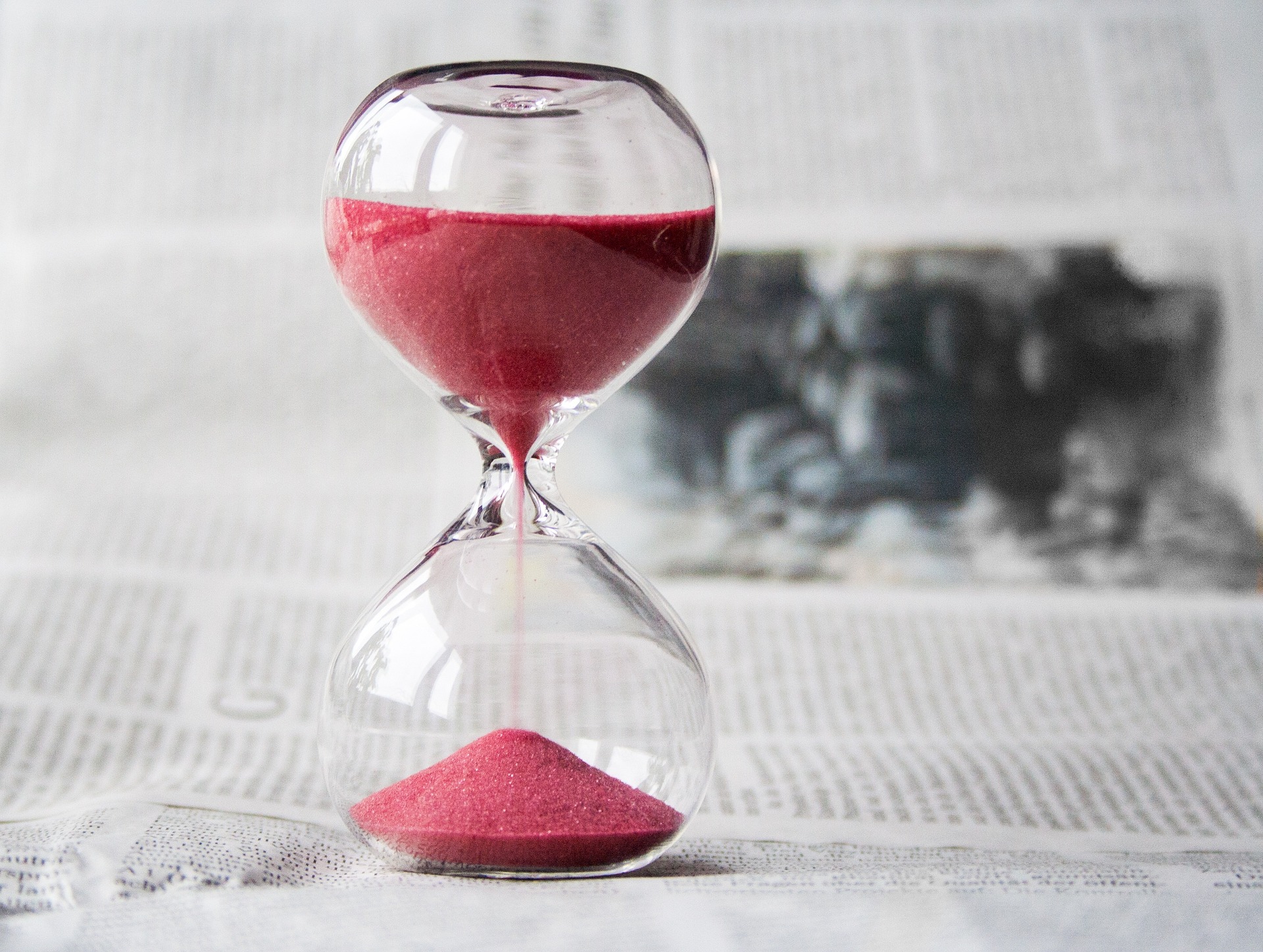 Hourglass with pink sand on a newspaper, a metaphor for the time and patience needed in alimony negotiations, guided by a Baltimore County divorce lawyer through collaborative law